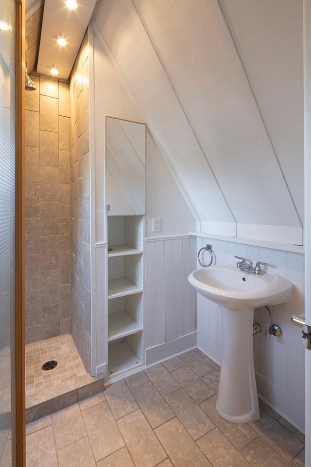 full bathroom with lofted ceiling, a shower stall, and wainscoting