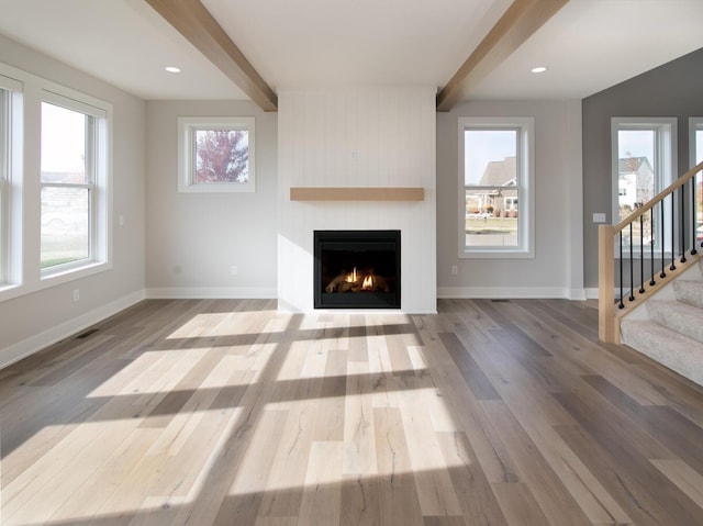 unfurnished living room with hardwood / wood-style floors, beam ceiling, a fireplace, and a wealth of natural light