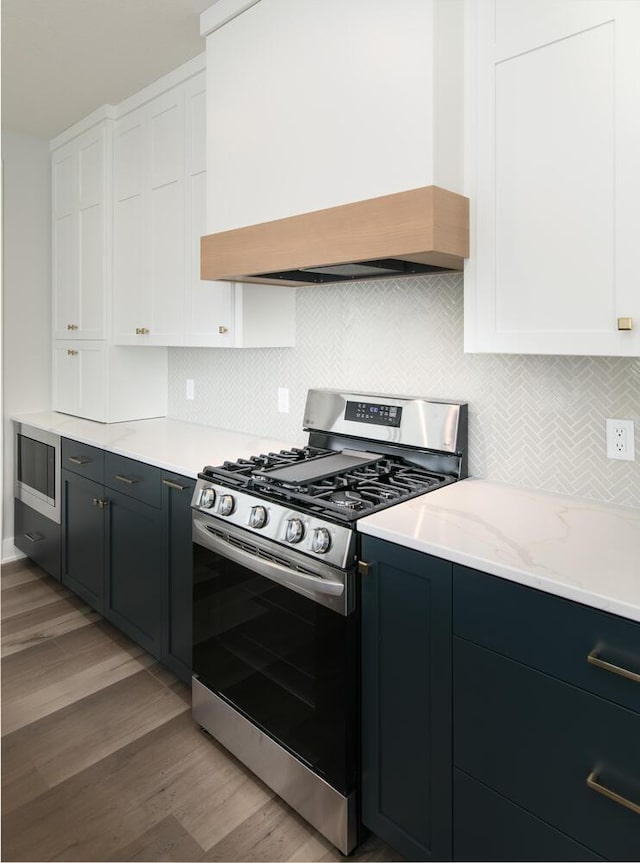 kitchen with white cabinets, custom range hood, appliances with stainless steel finishes, and light hardwood / wood-style flooring