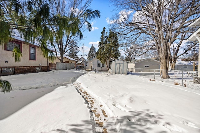 yard layered in snow with an outbuilding, a residential view, fence, and a storage shed