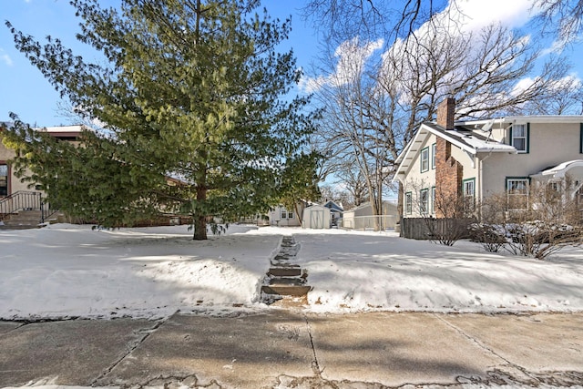 snowy yard featuring a storage shed, an outdoor structure, fence, and a residential view