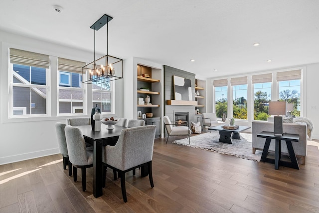 dining space with a large fireplace, a notable chandelier, dark hardwood / wood-style flooring, and built in shelves