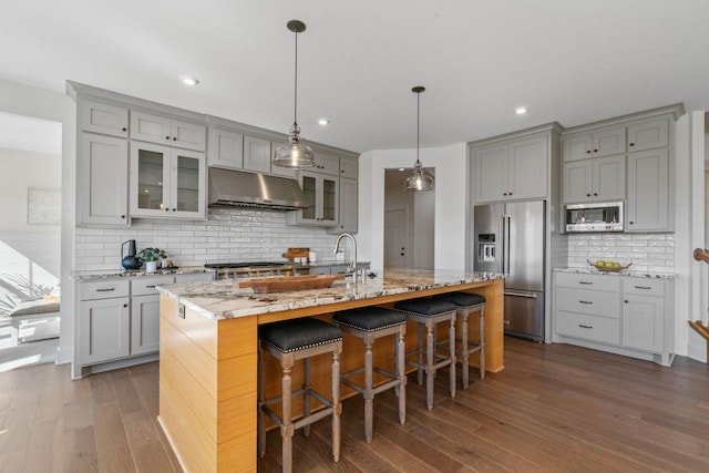 kitchen featuring a kitchen island with sink, stainless steel appliances, light stone countertops, a kitchen bar, and decorative backsplash