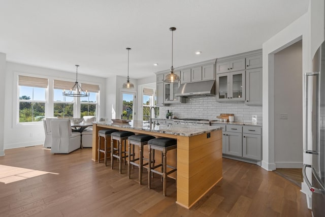 kitchen with a breakfast bar area, gray cabinetry, light stone counters, extractor fan, and an island with sink