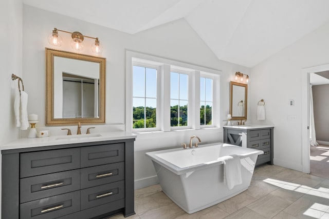 bathroom with tile patterned floors, lofted ceiling, a tub to relax in, and vanity