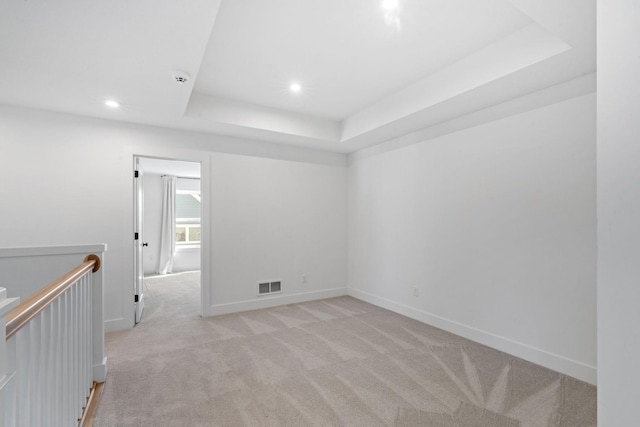 empty room with a raised ceiling and light colored carpet