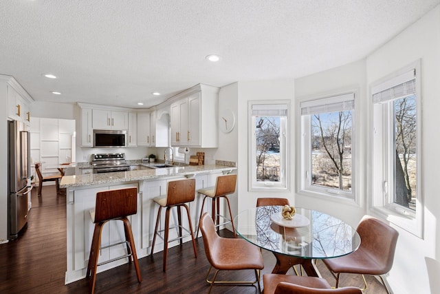 kitchen featuring dark wood-style floors, a peninsula, a sink, appliances with stainless steel finishes, and white cabinetry