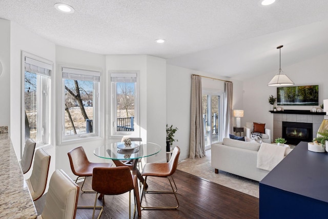 dining space with vaulted ceiling, recessed lighting, wood finished floors, and a tile fireplace