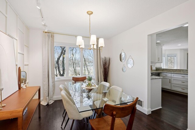 dining room with a chandelier, rail lighting, baseboards, and dark wood-style flooring