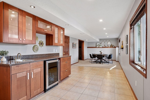 kitchen featuring a sink, glass insert cabinets, brown cabinets, and beverage cooler