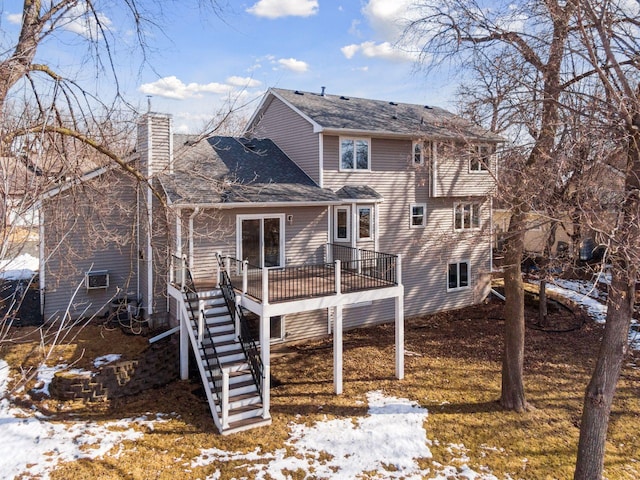 snow covered property featuring a wooden deck, stairway, a chimney, and a shingled roof