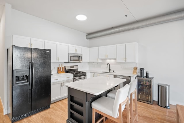 kitchen with a kitchen breakfast bar, sink, light wood-type flooring, appliances with stainless steel finishes, and white cabinetry