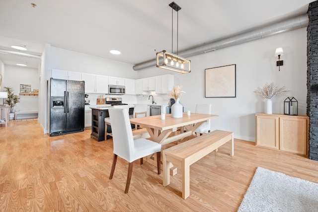 dining room featuring sink, a towering ceiling, and light hardwood / wood-style floors