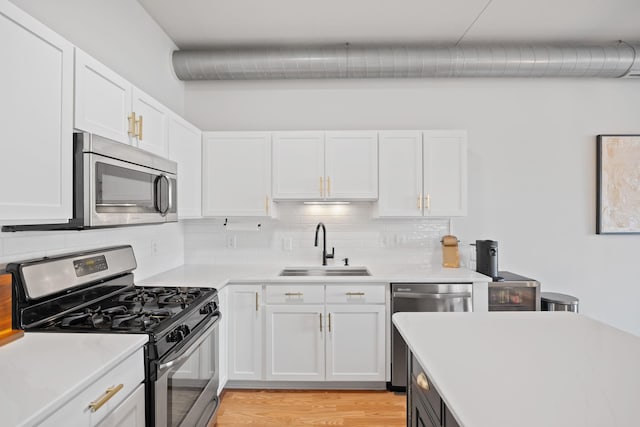 kitchen featuring light wood-type flooring, tasteful backsplash, stainless steel appliances, sink, and white cabinetry