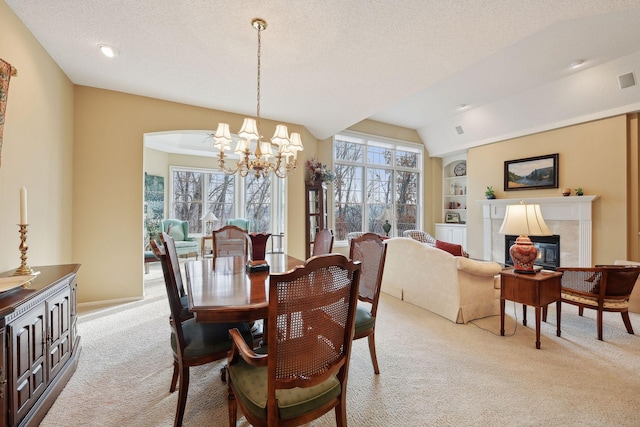 dining area with a tile fireplace, vaulted ceiling, built in features, light colored carpet, and a chandelier