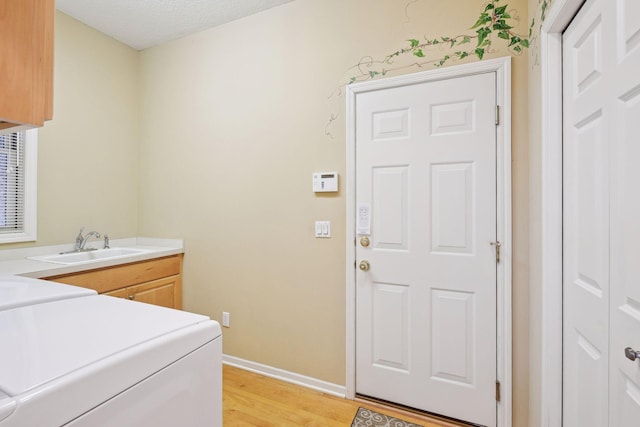 laundry area with sink, cabinets, separate washer and dryer, light hardwood / wood-style floors, and a textured ceiling