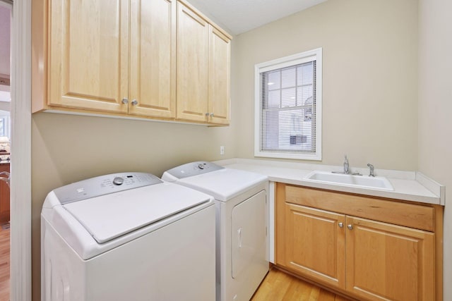 laundry room with washing machine and clothes dryer, sink, cabinets, and light hardwood / wood-style floors