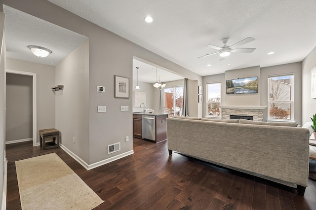 living room with dark wood-type flooring, a stone fireplace, sink, a textured ceiling, and a wealth of natural light