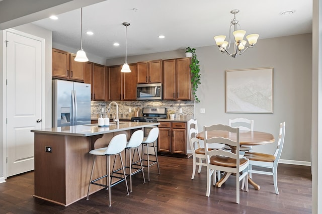 kitchen featuring pendant lighting, stainless steel appliances, a kitchen breakfast bar, tasteful backsplash, and a center island with sink