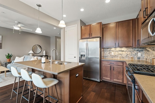 kitchen with pendant lighting, an island with sink, sink, backsplash, and stainless steel appliances