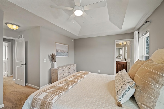 carpeted bedroom with ceiling fan, a tray ceiling, and ensuite bath