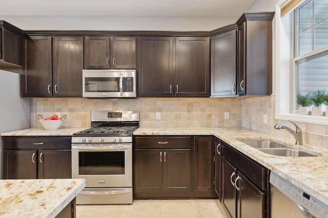 kitchen featuring appliances with stainless steel finishes, decorative backsplash, light stone countertops, dark brown cabinetry, and sink