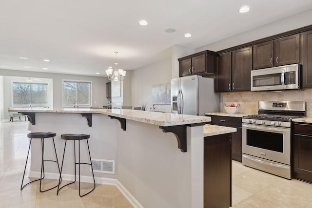 kitchen featuring decorative light fixtures, a kitchen island, appliances with stainless steel finishes, a breakfast bar area, and light stone counters