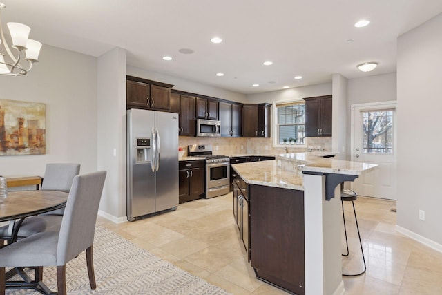 kitchen featuring light stone countertops, pendant lighting, appliances with stainless steel finishes, a center island, and dark brown cabinetry