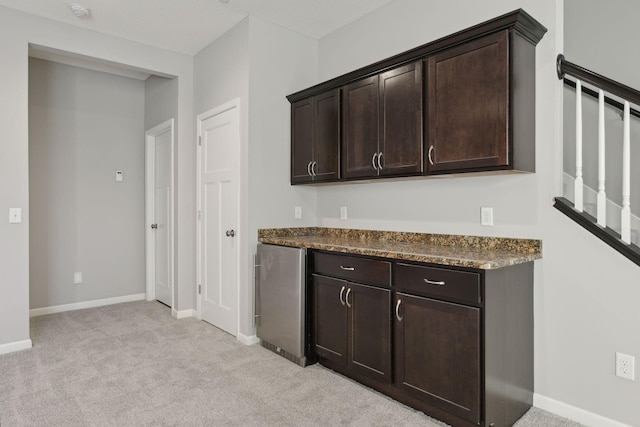 kitchen featuring light carpet, dark brown cabinets, stainless steel fridge, and dark stone countertops