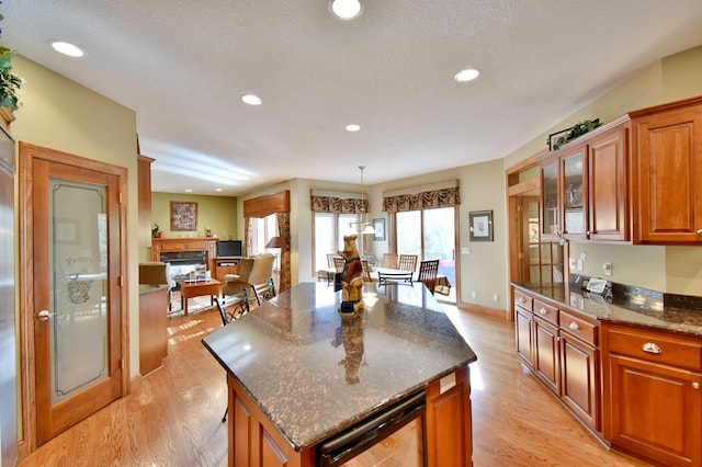 kitchen with light wood-type flooring, dark stone counters, pendant lighting, a center island, and a stone fireplace