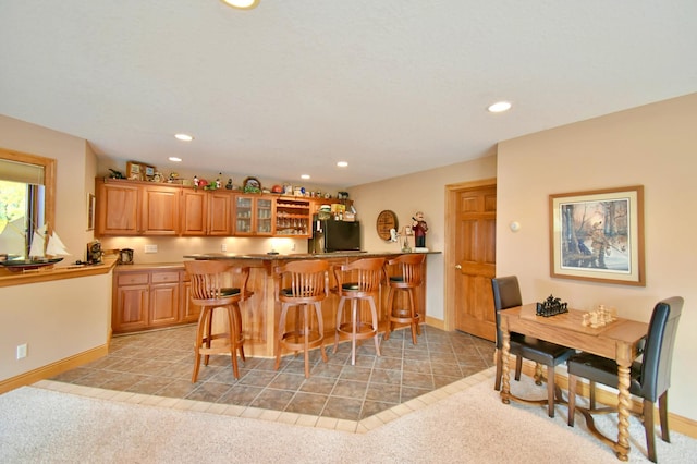 kitchen with a breakfast bar, kitchen peninsula, black fridge, and light colored carpet