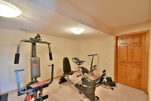 exercise area featuring light colored carpet and a textured ceiling