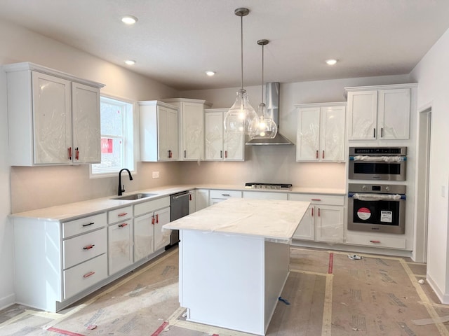 kitchen with a kitchen island, sink, white cabinets, hanging light fixtures, and wall chimney range hood