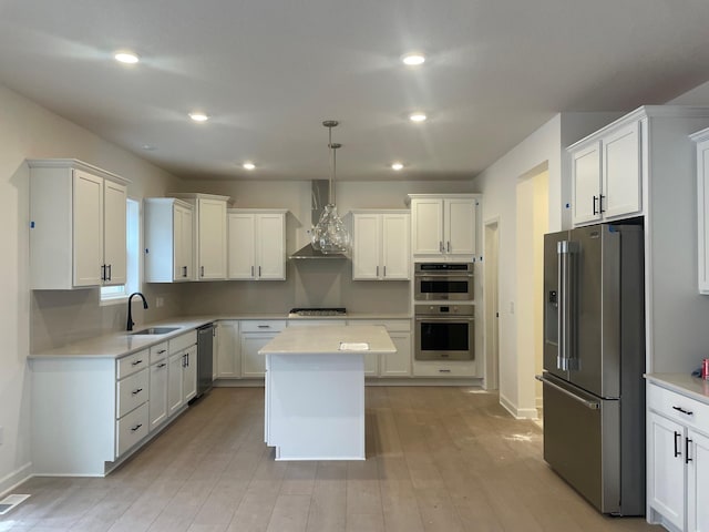 kitchen with stainless steel appliances, decorative light fixtures, white cabinets, and wall chimney exhaust hood