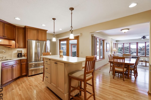 kitchen with a kitchen island, pendant lighting, sink, stainless steel fridge, and decorative backsplash