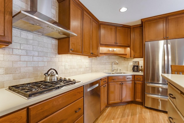 kitchen with sink, appliances with stainless steel finishes, tasteful backsplash, light hardwood / wood-style floors, and wall chimney exhaust hood