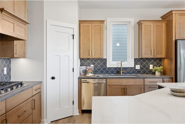 kitchen with appliances with stainless steel finishes, light brown cabinets, backsplash, and a sink
