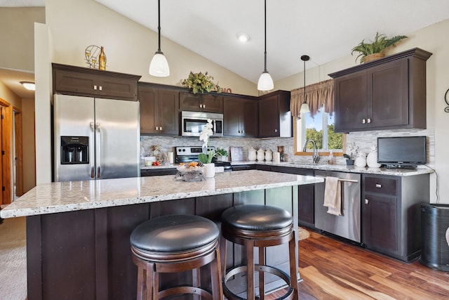 kitchen with appliances with stainless steel finishes, lofted ceiling, hanging light fixtures, a center island, and dark brown cabinetry