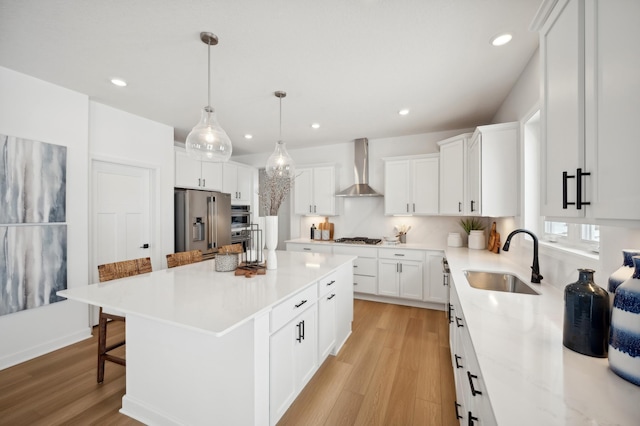 kitchen featuring wall chimney range hood, a breakfast bar area, white cabinetry, a center island, and decorative light fixtures