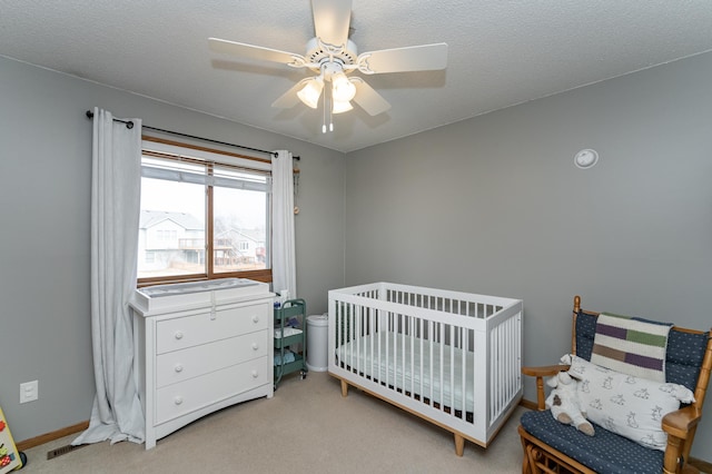 bedroom with ceiling fan, a textured ceiling, carpet flooring, baseboards, and a crib