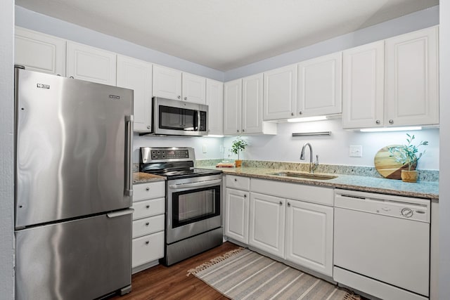 kitchen with appliances with stainless steel finishes, sink, white cabinets, dark wood-type flooring, and light stone counters