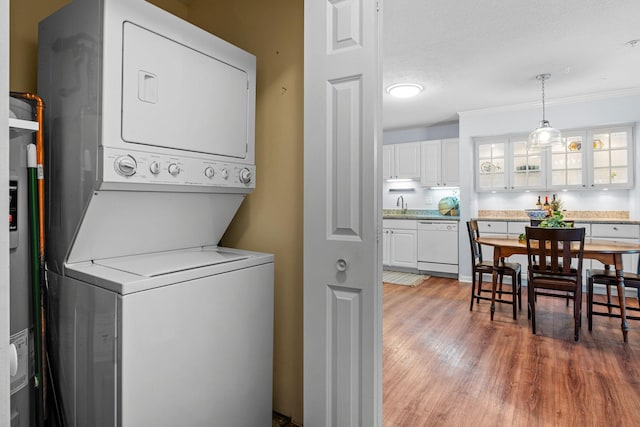 clothes washing area featuring sink, stacked washer / drying machine, a textured ceiling, and wood-type flooring