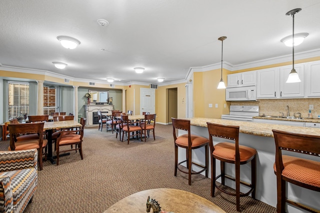 kitchen with white appliances, white cabinetry, hanging light fixtures, carpet flooring, and crown molding