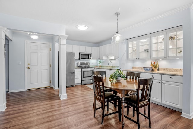 dining room featuring light wood-style floors, baseboards, crown molding, and ornate columns