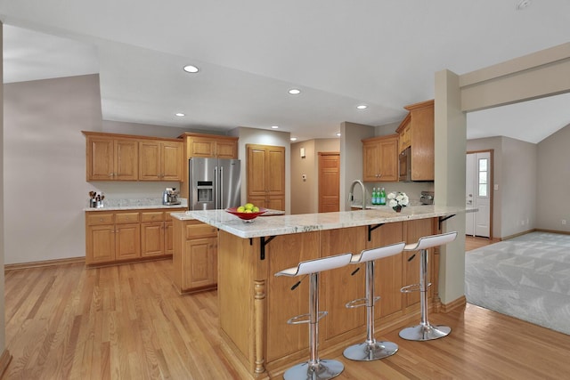 kitchen featuring a kitchen breakfast bar, light stone counters, light hardwood / wood-style flooring, kitchen peninsula, and stainless steel fridge