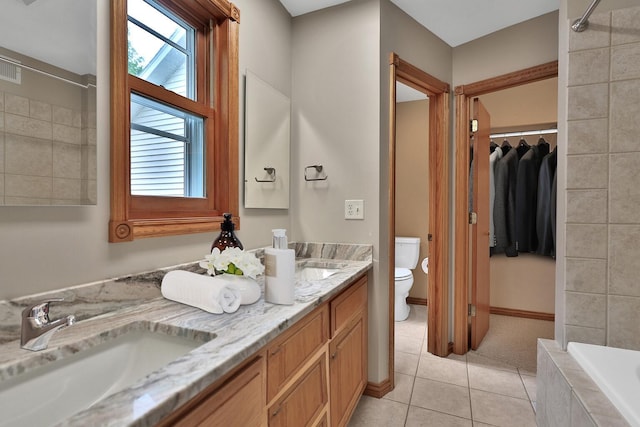 bathroom with tile patterned floors, vanity, a relaxing tiled tub, and toilet