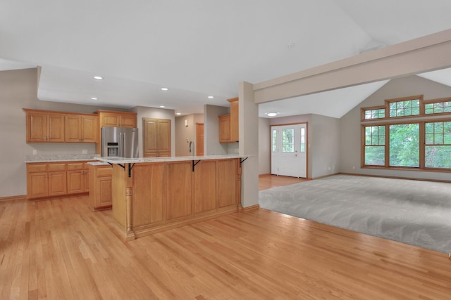 kitchen featuring a kitchen breakfast bar, light hardwood / wood-style flooring, kitchen peninsula, stainless steel fridge, and vaulted ceiling