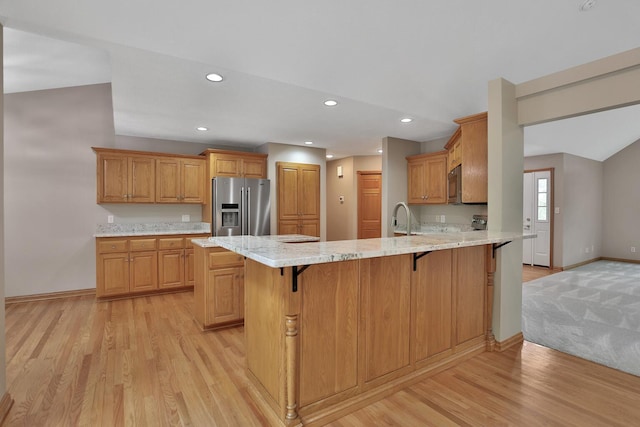 kitchen with kitchen peninsula, stainless steel fridge, light stone counters, light hardwood / wood-style floors, and a breakfast bar area