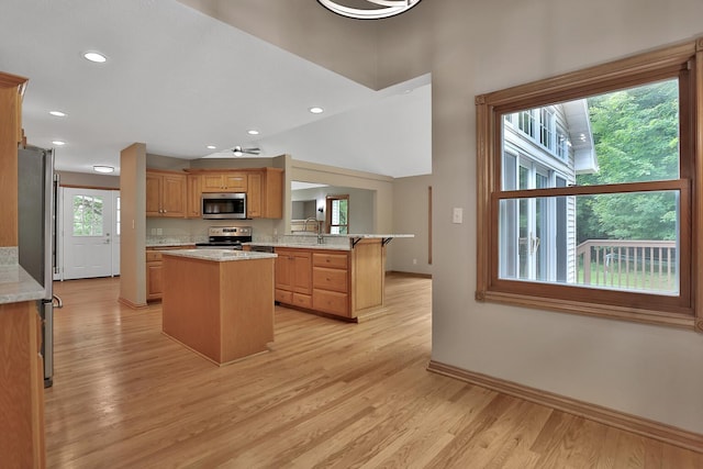 kitchen featuring a center island, light wood-type flooring, light stone counters, kitchen peninsula, and stainless steel appliances