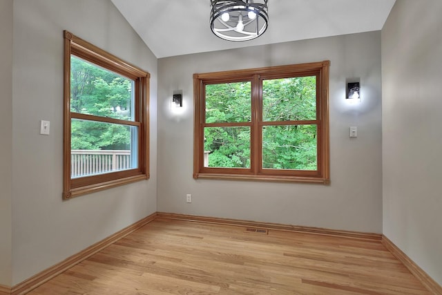 empty room featuring an inviting chandelier, lofted ceiling, and light wood-type flooring